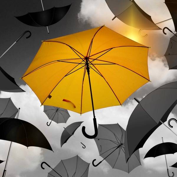 Gelber Regenschirm schwebt unter mehreren schwarz-weißen Regenschirmen vor bewölktem Himmel